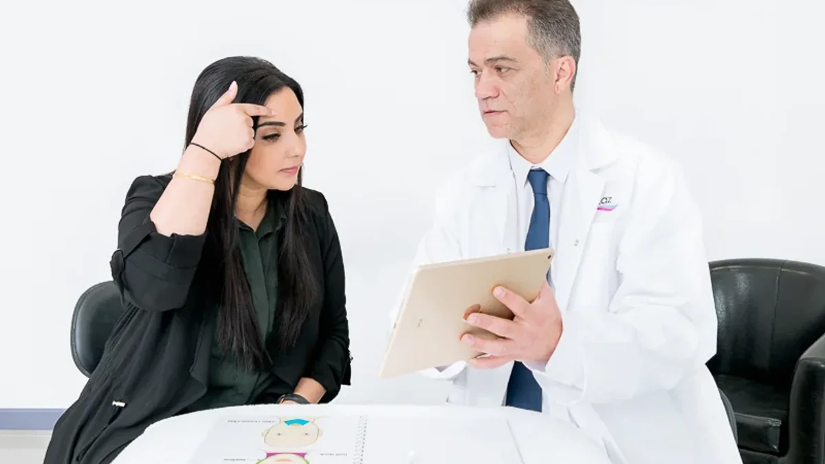 A CoLaz clinician in branded uniform talks a patient through anti-wrinkle aftercare at a calm, softly lit consultation desk